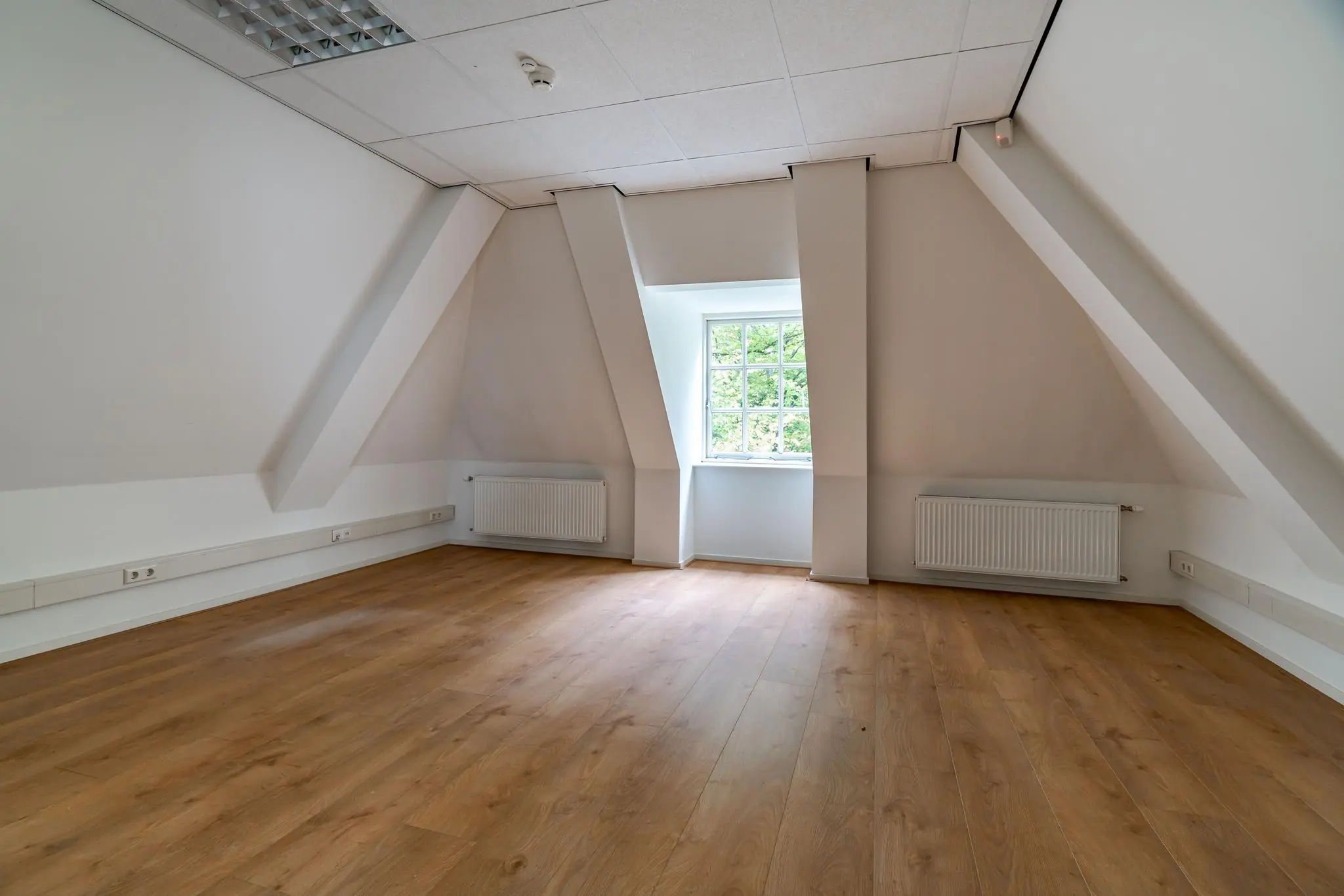 Lege zolderkamer met laminaatvloer, schuine wanden en een raam aan het Lange Voorhout.